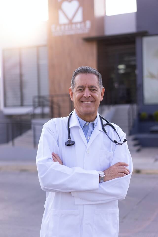 Middle aged consultant doctor wearing labcoat standing in front of large hospital health center